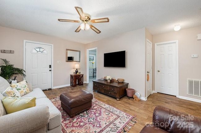 living room with a textured ceiling, wood-type flooring, and ceiling fan