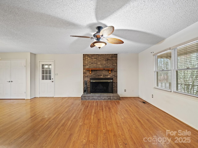 unfurnished living room with ceiling fan, a textured ceiling, a fireplace, and light hardwood / wood-style floors