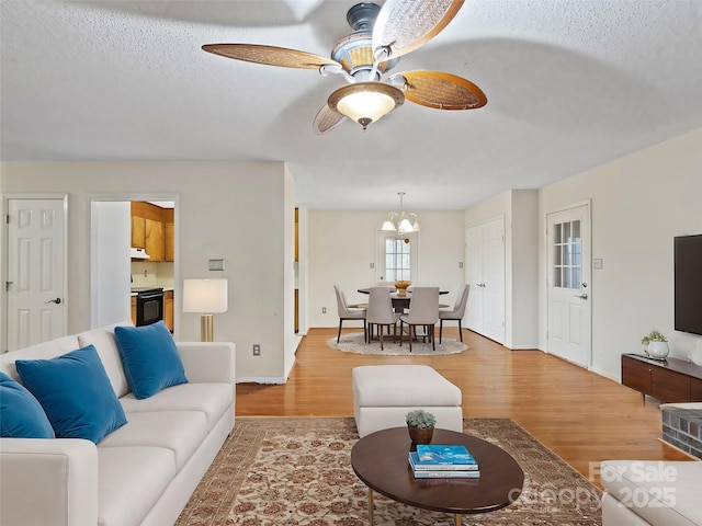 living area featuring baseboards, light wood-style floors, a textured ceiling, and ceiling fan with notable chandelier