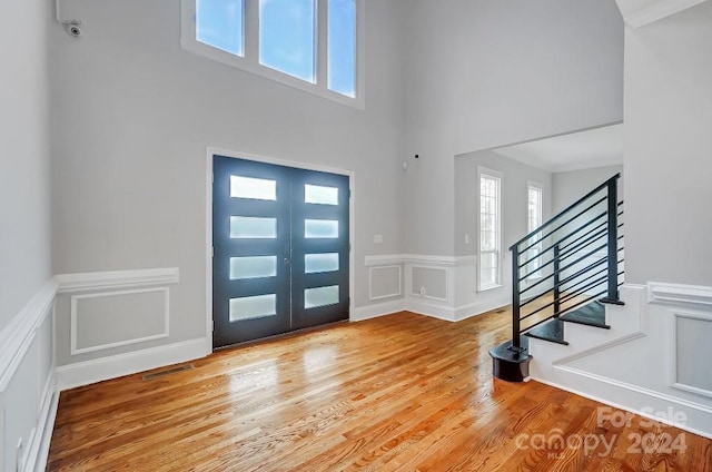 foyer entrance featuring plenty of natural light, light hardwood / wood-style floors, a towering ceiling, and french doors