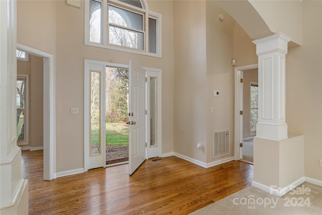 foyer with ornate columns, a towering ceiling, and light hardwood / wood-style floors