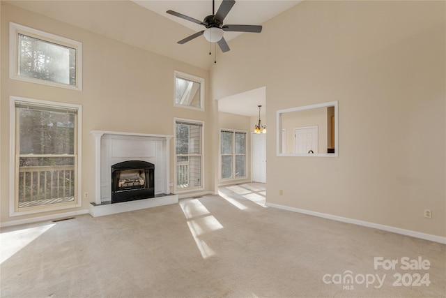 unfurnished living room with ceiling fan with notable chandelier, light colored carpet, and high vaulted ceiling