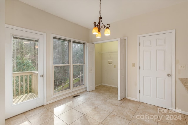 doorway to outside with a notable chandelier, light tile patterned floors, and a wealth of natural light