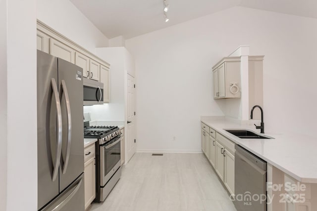 kitchen featuring sink, kitchen peninsula, cream cabinets, vaulted ceiling, and appliances with stainless steel finishes