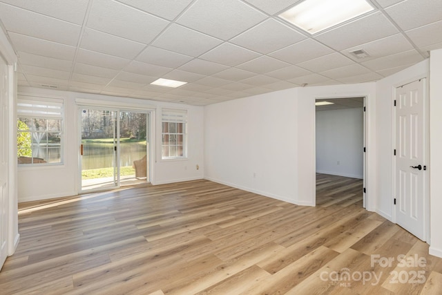 spare room featuring light wood-type flooring, a water view, and a drop ceiling