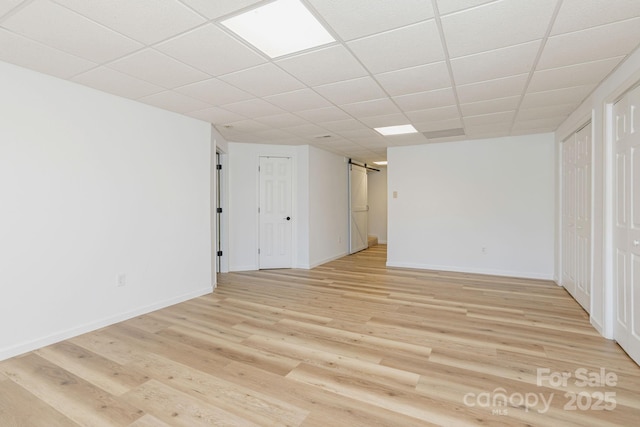 interior space with a drop ceiling, a barn door, and light hardwood / wood-style flooring