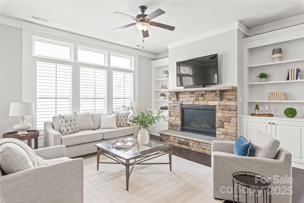 living area with visible vents, ceiling fan, crown molding, built in shelves, and a fireplace