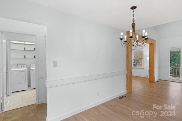 unfurnished dining area featuring light wood-type flooring, an inviting chandelier, and washer and clothes dryer