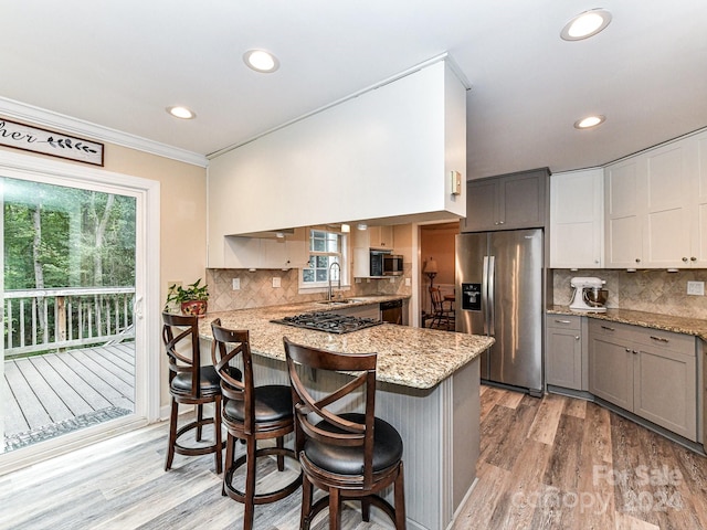 kitchen featuring kitchen peninsula, appliances with stainless steel finishes, a breakfast bar, and gray cabinets