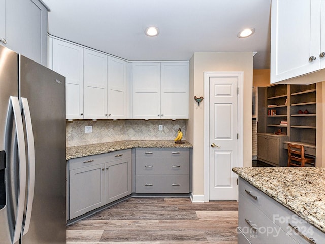 kitchen featuring white cabinetry, light stone countertops, light hardwood / wood-style flooring, stainless steel fridge, and decorative backsplash