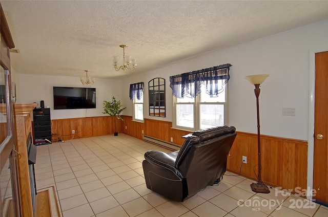 tiled living room featuring baseboard heating, wood walls, a chandelier, and a textured ceiling