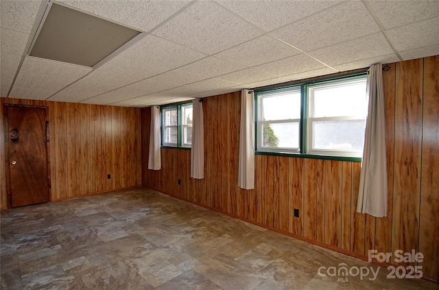 unfurnished room featuring a paneled ceiling and wood walls