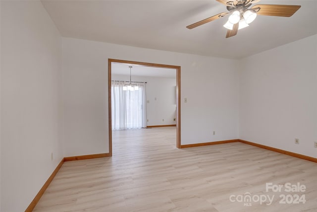 unfurnished room with ceiling fan with notable chandelier and light hardwood / wood-style flooring