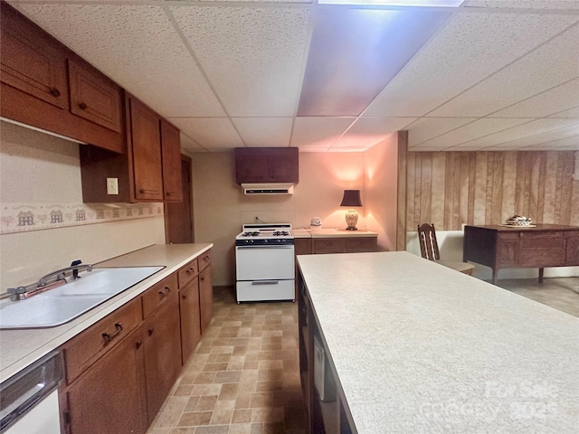 kitchen with sink, wooden walls, white gas range, dishwasher, and a drop ceiling