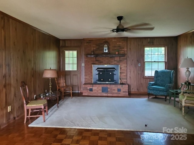 living room with a ceiling fan, a brick fireplace, wooden walls, and a healthy amount of sunlight