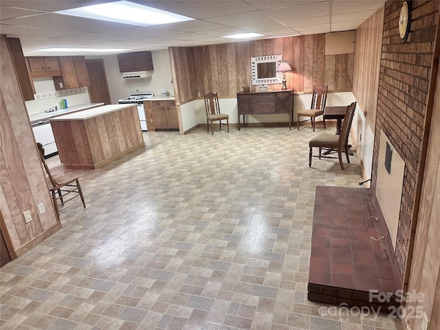 kitchen featuring wood walls, a kitchen island, a drop ceiling, white gas range, and light countertops