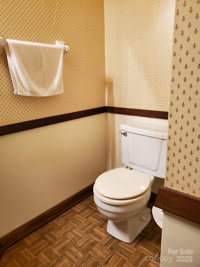 half bathroom featuring baseboards, toilet, and wallpapered walls