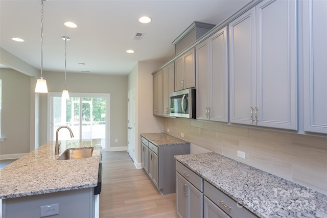 kitchen with pendant lighting, sink, light stone countertops, an island with sink, and tasteful backsplash