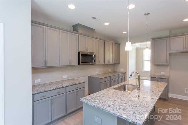 kitchen featuring a center island with sink, sink, hanging light fixtures, gray cabinets, and light hardwood / wood-style floors