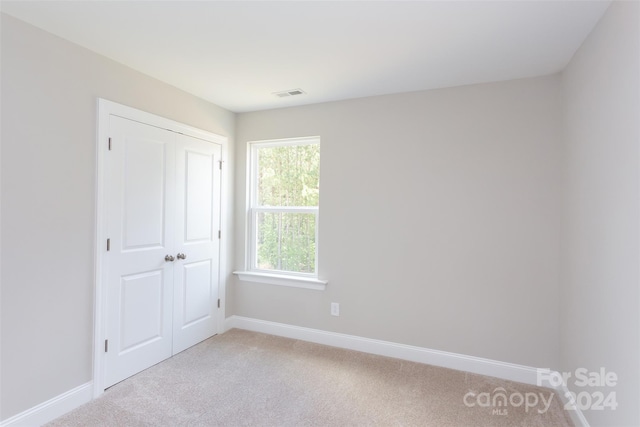 unfurnished bedroom with light carpet and a closet