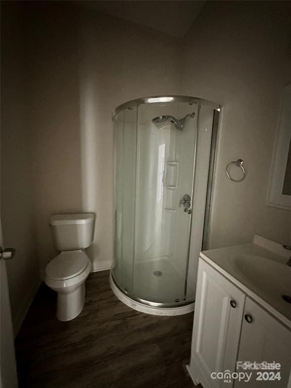 bathroom with hardwood / wood-style flooring, vanity, toilet, and a shower with shower door