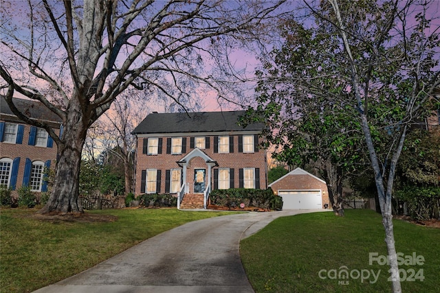 colonial-style house featuring a garage, an outdoor structure, and a lawn