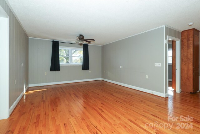 unfurnished room featuring ceiling fan, light hardwood / wood-style flooring, wooden walls, and ornamental molding