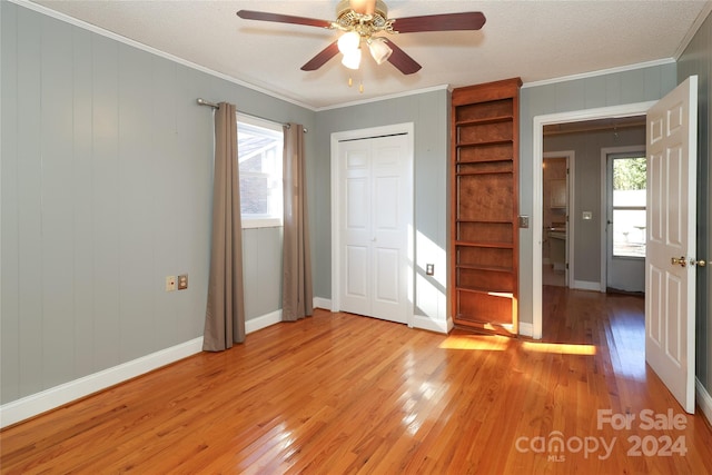 unfurnished bedroom featuring light wood-type flooring, ornamental molding, a textured ceiling, ceiling fan, and a closet