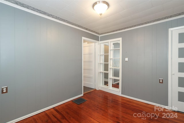 unfurnished room featuring wood-type flooring, crown molding, and wood walls