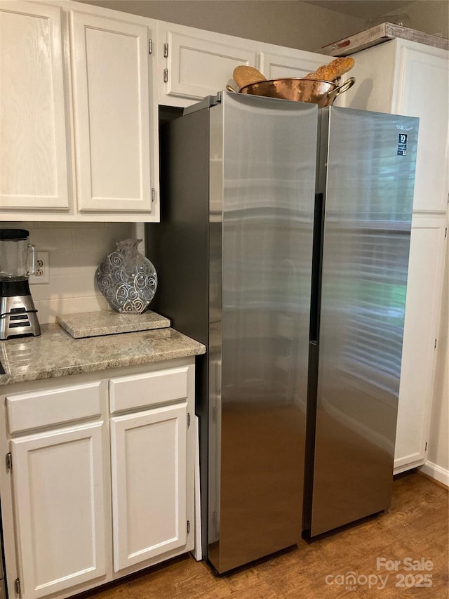 kitchen with light hardwood / wood-style floors, stainless steel fridge, white cabinetry, and backsplash