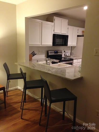 kitchen with dark wood-type flooring, a kitchen breakfast bar, kitchen peninsula, stainless steel electric range, and white cabinets