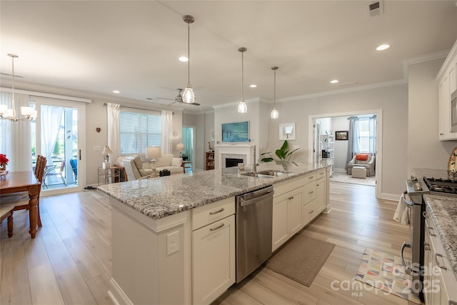 kitchen with stainless steel appliances, sink, white cabinets, hanging light fixtures, and an island with sink