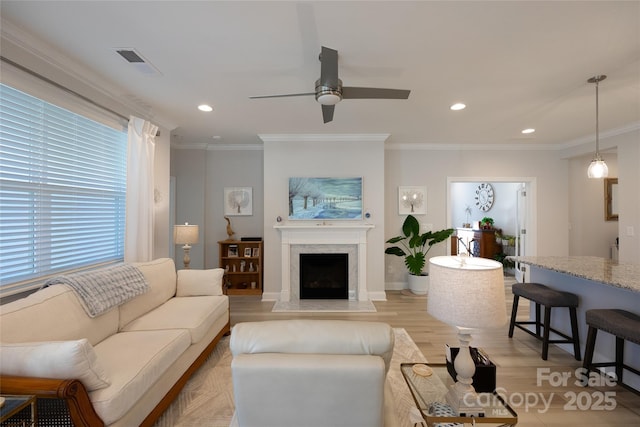 living room featuring a high end fireplace, light wood-type flooring, and ornamental molding