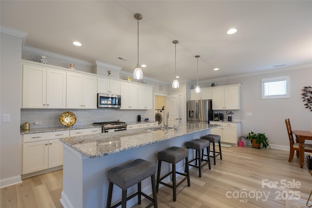 kitchen featuring white cabinets, hanging light fixtures, an island with sink, appliances with stainless steel finishes, and a kitchen bar