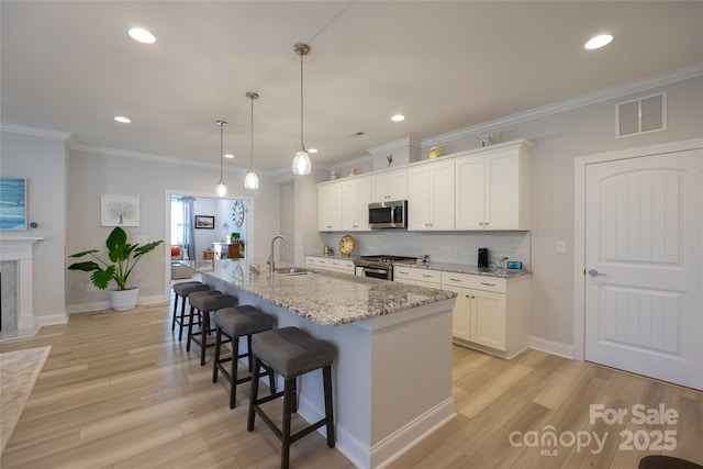 kitchen with white cabinets, a kitchen island with sink, sink, and appliances with stainless steel finishes