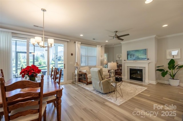 living room featuring ceiling fan with notable chandelier, light hardwood / wood-style floors, crown molding, and a premium fireplace