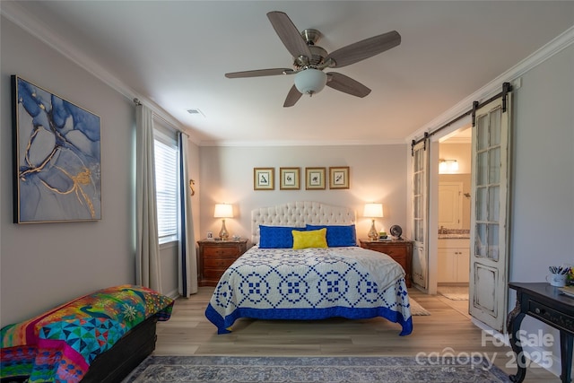 bedroom featuring a barn door, ceiling fan, crown molding, and connected bathroom