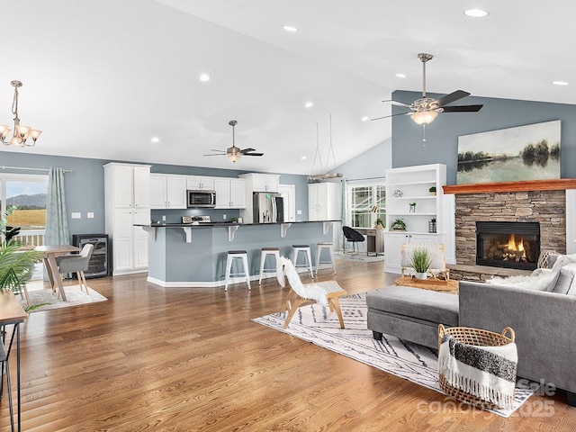 living room featuring lofted ceiling, a fireplace, hardwood / wood-style floors, and ceiling fan with notable chandelier