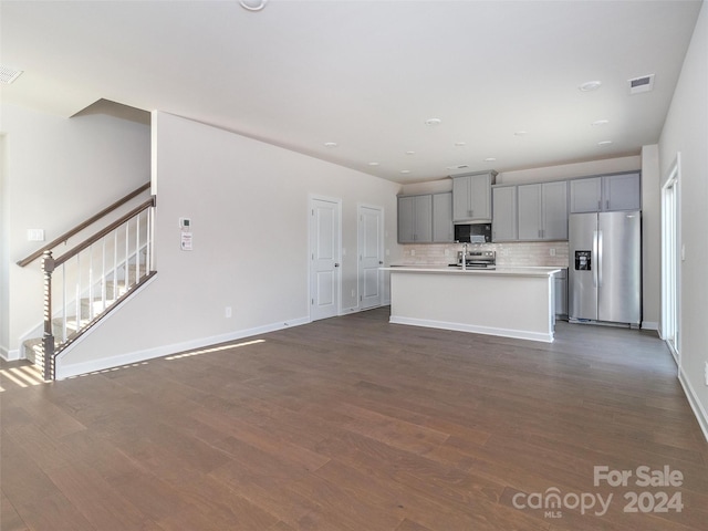 kitchen featuring gray cabinetry, stainless steel appliances, dark hardwood / wood-style flooring, backsplash, and a kitchen island with sink