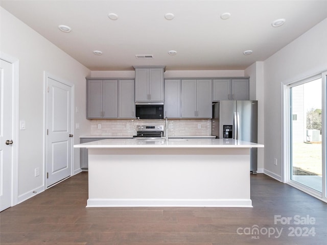 kitchen with appliances with stainless steel finishes, backsplash, gray cabinets, and a center island with sink