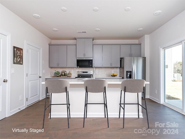 kitchen featuring a kitchen breakfast bar, gray cabinets, appliances with stainless steel finishes, and tasteful backsplash