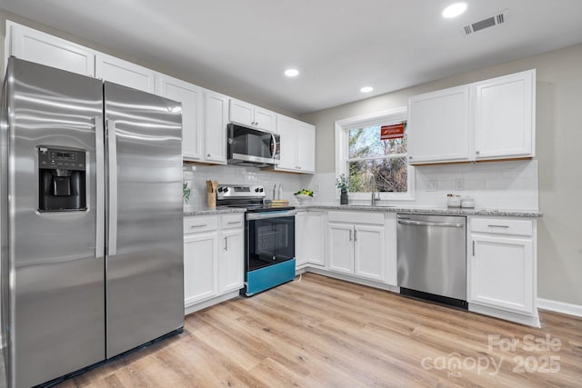 kitchen with light wood-type flooring, backsplash, light stone counters, stainless steel appliances, and white cabinets