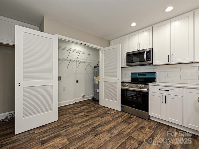 kitchen with light countertops, water heater, appliances with stainless steel finishes, dark wood-type flooring, and white cabinets