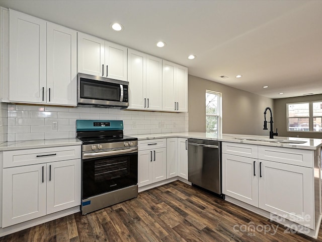 kitchen with a peninsula, a sink, white cabinets, light countertops, and appliances with stainless steel finishes