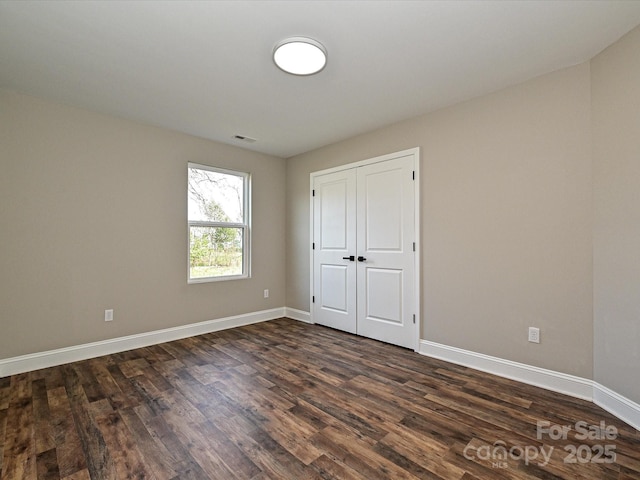 unfurnished bedroom featuring dark wood-style flooring, visible vents, and baseboards