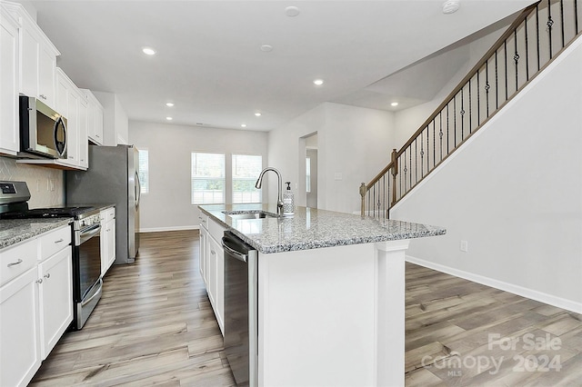 kitchen with light stone counters, sink, appliances with stainless steel finishes, and an island with sink