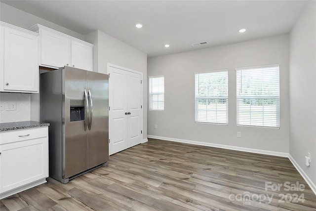 kitchen featuring white cabinets, dark stone countertops, tasteful backsplash, light hardwood / wood-style floors, and stainless steel fridge with ice dispenser