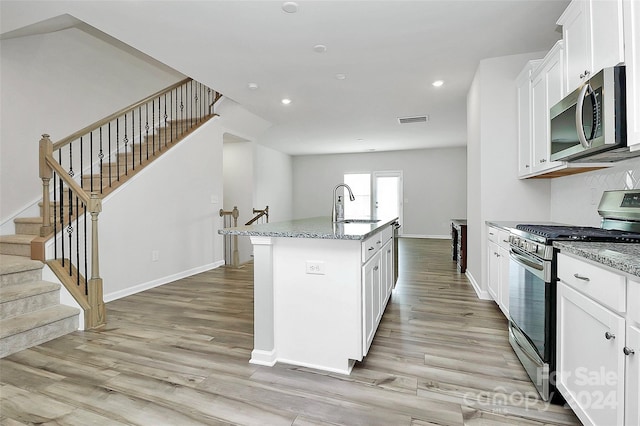 kitchen with light stone countertops, stainless steel appliances, white cabinets, and an island with sink