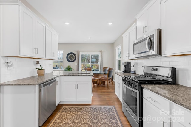 kitchen with white cabinetry, kitchen peninsula, stone countertops, appliances with stainless steel finishes, and hardwood / wood-style flooring