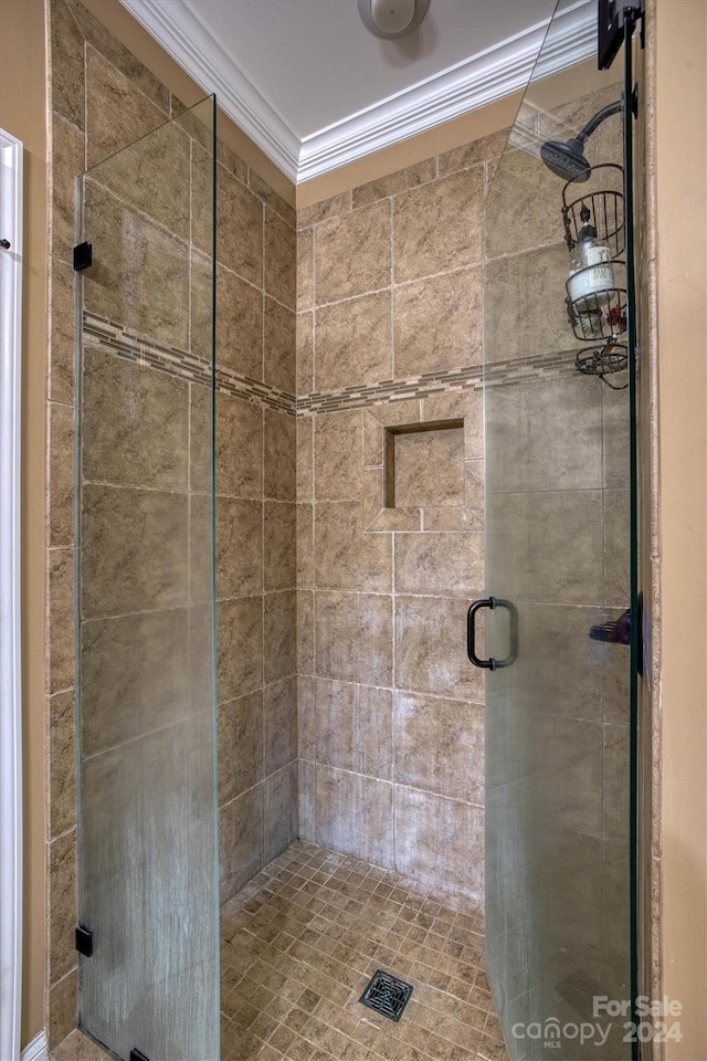 bathroom with a shower with shower door and ornamental molding